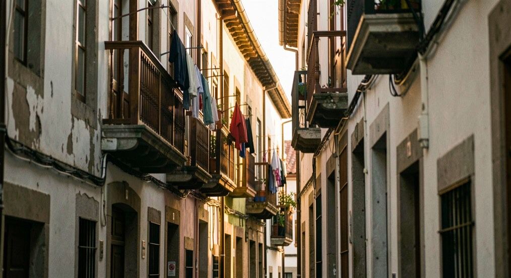 Calle estrecha de Bilbao al atardecer con balcones de madera, ropa tendida y una luz dorada entrando entre los edificios antiguos.